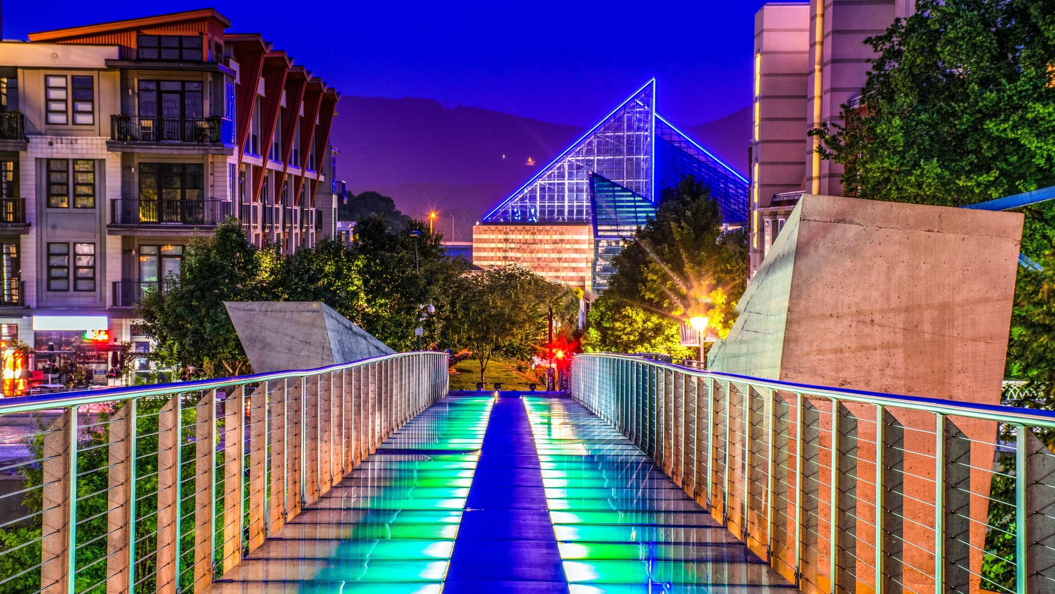 The Holmberg Glass Bridge lit at dusk, looking toward the Tennessee Aquarium in downtown Chattanooga